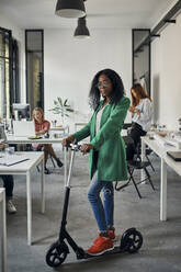 Portrait of a businesswoman with kick scooter in office - ZEDF02829