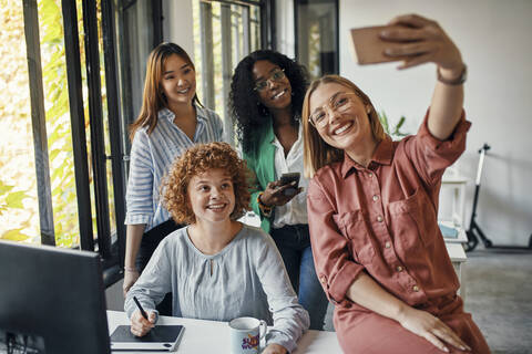 Glückliche Kolleginnen machen ein Selfie im Büro, lizenzfreies Stockfoto