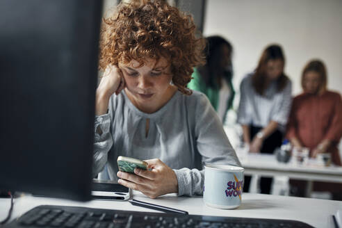 Businesswoman using smartphone at desk in office - ZEDF02840