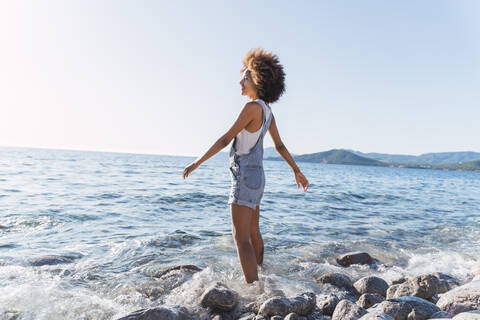 Rückansicht einer jungen Frau am Strand, Blick in die Ferne, lizenzfreies Stockfoto