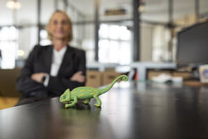 Mature businesswoman with chameleon figurine on desk in office - GUSF02700