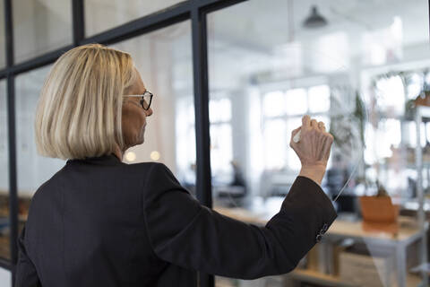 Reife Geschäftsfrau zeichnet auf Glasscheibe im Büro, lizenzfreies Stockfoto