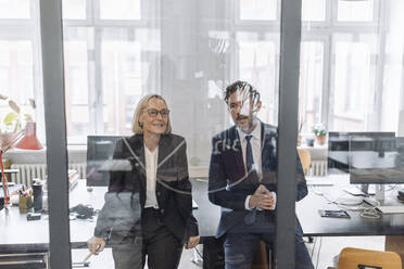 Businessman and businesswoman looking at drawing on glass pane in office - GUSF02704