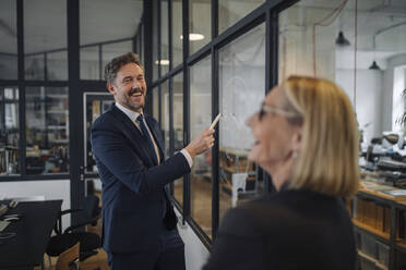 Businessman and businesswoman looking at drawing on glass pane in office - GUSF02707