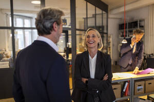 Smiling businesswoman and businessman talking in office - GUSF02713