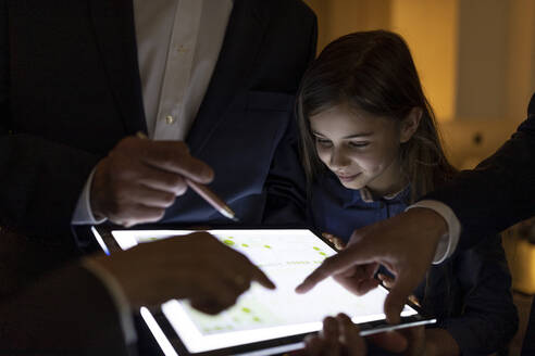 Geschäftsleute und ein Mädchen betrachten einen glänzenden Bauplan auf einem Tablet im Büro - GUSF02720