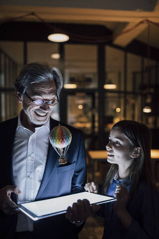 Happy senior buisinessman and girl with hot-air balloon and shining tablet in office stock photo