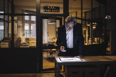 Älterer Geschäftsmann schaut auf ein leuchtendes Tablet im Büro - GUSF02729