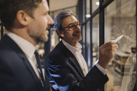 Zwei Geschäftsleute arbeiten an einer Zeichnung auf einer Glasscheibe im Büro, lizenzfreies Stockfoto