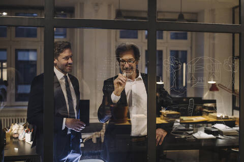 Zwei Geschäftsleute arbeiten an einer Zeichnung auf einer Glasscheibe im Büro, lizenzfreies Stockfoto