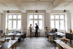 Businessman and businesswoman talking at the window in office - GUSF02764