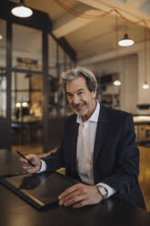Porträt eines lächelnden älteren Geschäftsmannes, der ein Grafiktablett am Schreibtisch im Büro benutzt - GUSF02771