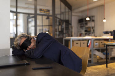 Senior businessman having a power nap at desk in office - GUSF02779