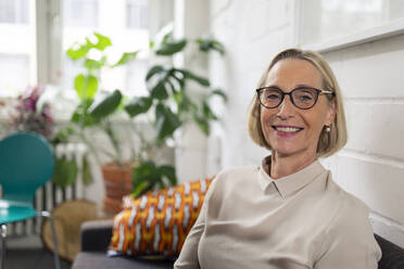 Portrait of smiling mature businesswoman on couch in office lounge - GUSF02783