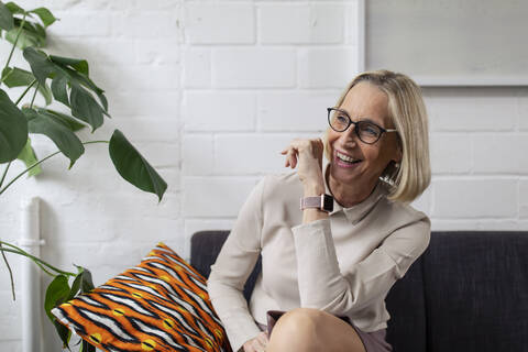 Happy mature businesswoman with smartwatch sitting on couch in office lounge stock photo