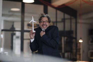 Freezing senior businessman holding wind turbine model in office - GUSF02803