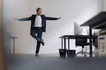 Senior businessman doing a yoga exercise in office - GUSF02808