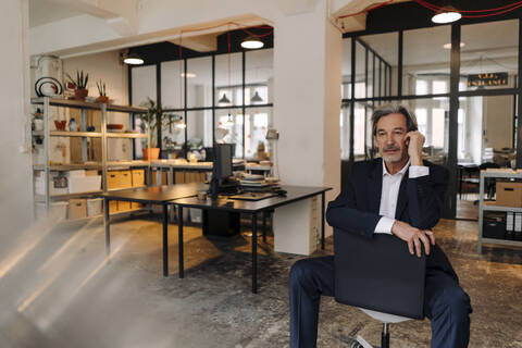 Älterer Geschäftsmann sitzt auf einem Stuhl im Büro, lizenzfreies Stockfoto