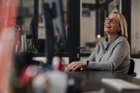 Happy mature businesswoman sitting at desk in office stock photo