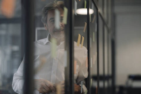 Senior businessman looking at adhesive notes at glass pane in office stock photo