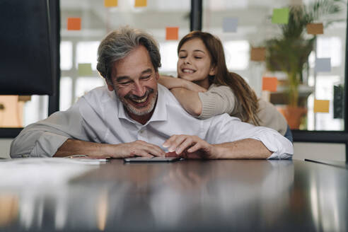 Happy senior buisinessman and girl looking at tablet in office - GUSF02859