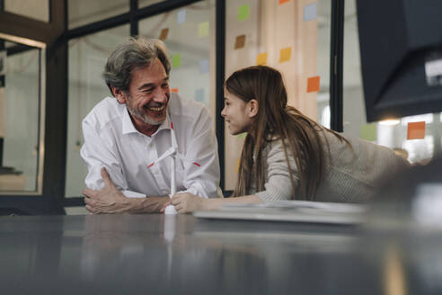 Happy senior buisinessman and girl with wind turbine model in office - GUSF02861