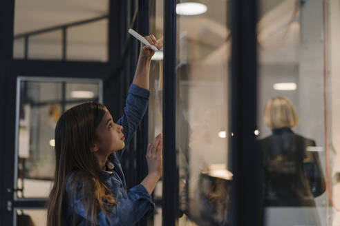 Girl drawing on glass pane in office - GUSF02877