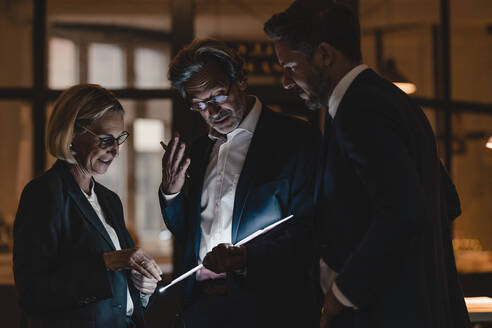 Geschäftsleute mit leuchtendem Tablet im Gespräch im Büro - GUSF02894