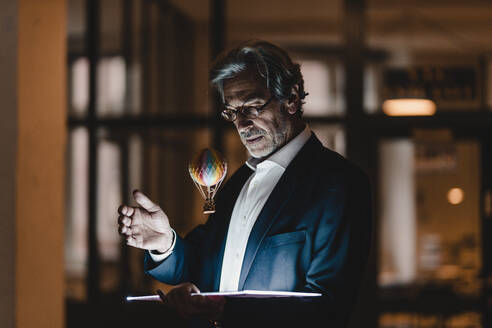 Älterer Geschäftsmann mit Tablet und schwebendem Heißluftballon im Büro - GUSF02899