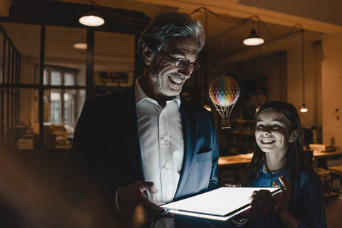 Happy senior buisinessman and girl with hot-air balloon and shining tablet in office stock photo