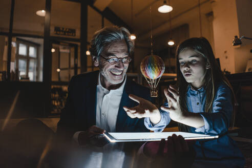 Happy senior buisinessman and girl with hot-air balloon and shining tablet in office - GUSF02906