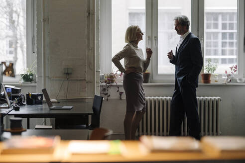 Geschäftsmann und Geschäftsfrau im Gespräch am Fenster im Büro - GUSF02911