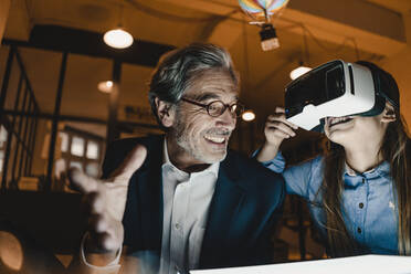 Happy senior buisinessman and girl wearing VR glasses with hot-air balloon in office - GUSF02912