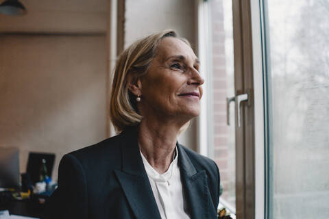 Mature businesswoman looking out of window in office stock photo