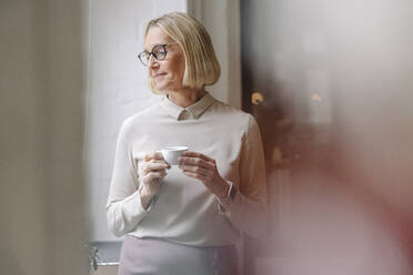 Ältere Geschäftsfrau macht eine Kaffeepause am Fenster im Büro - GUSF02929