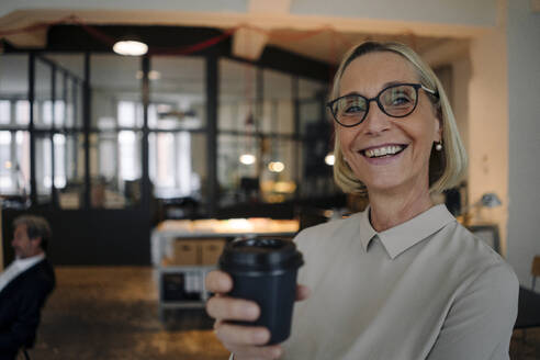 Portrait of happy mature businesswoman having a coffee break in office - GUSF02932