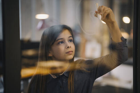 Girl drawing on glass pane in office - GUSF02943