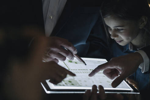 Geschäftsleute und ein Mädchen betrachten einen glänzenden Bauplan auf einem Tablet im Büro - GUSF02946
