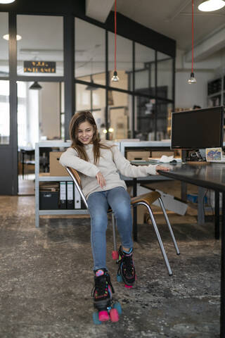 Girl with roller skates sitting at desk in office wobbling with chair stock photo