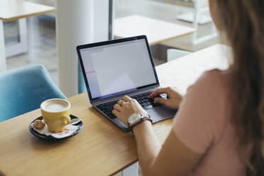 Studentin beim Tippen auf ihrem Computer im Café - MOMF00811