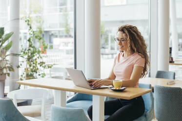 Junge Studentin bei der Arbeit an ihrem Laptop in einem Café - MOMF00813