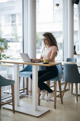 Junge Studentin bei der Arbeit an ihrem Laptop in einem Café - MOMF00815
