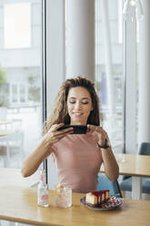 Young student taking a picture of her cake at coffee shop - MOMF00819