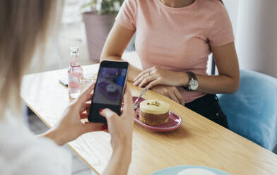 Junge Frau fotografiert ihren Kuchen in einem Café - MOMF00820