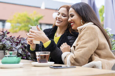 Zwei Freundinnen benutzen ihr Smartphone im Freien in einem Café - ERRF02198