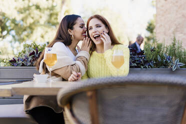 Zwei Freundinnen flüstern im Freien in einem Café - ERRF02204