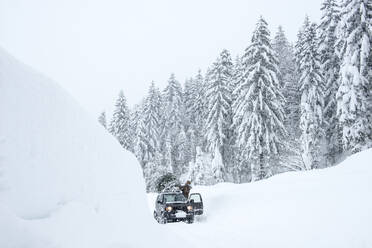 Austria, Salzburger Land, Lammertal, Man attaching Christmas tree to car roof on snowy road - HHF05579