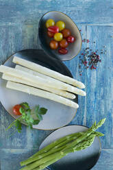 White and green asparagus on rustic wooden background, yellow tomatoes, red tomatoes, colored pepper, parsley - ASF06537