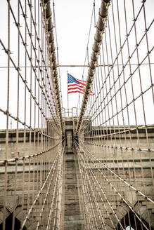 USA, New York, New York City, Seile der Brooklyn Bridge mit amerikanischer Flagge obenauf - CJMF00177