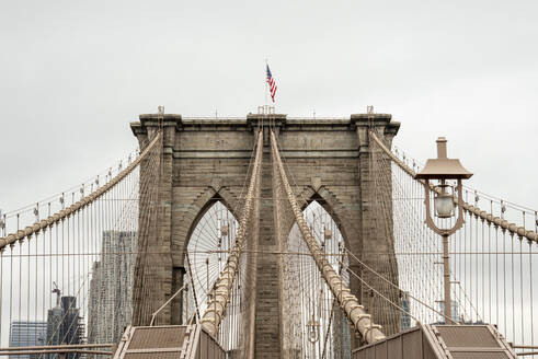 USA, New York, New York City, Seile der Brooklyn Bridge mit amerikanischer Flagge obenauf - CJMF00179